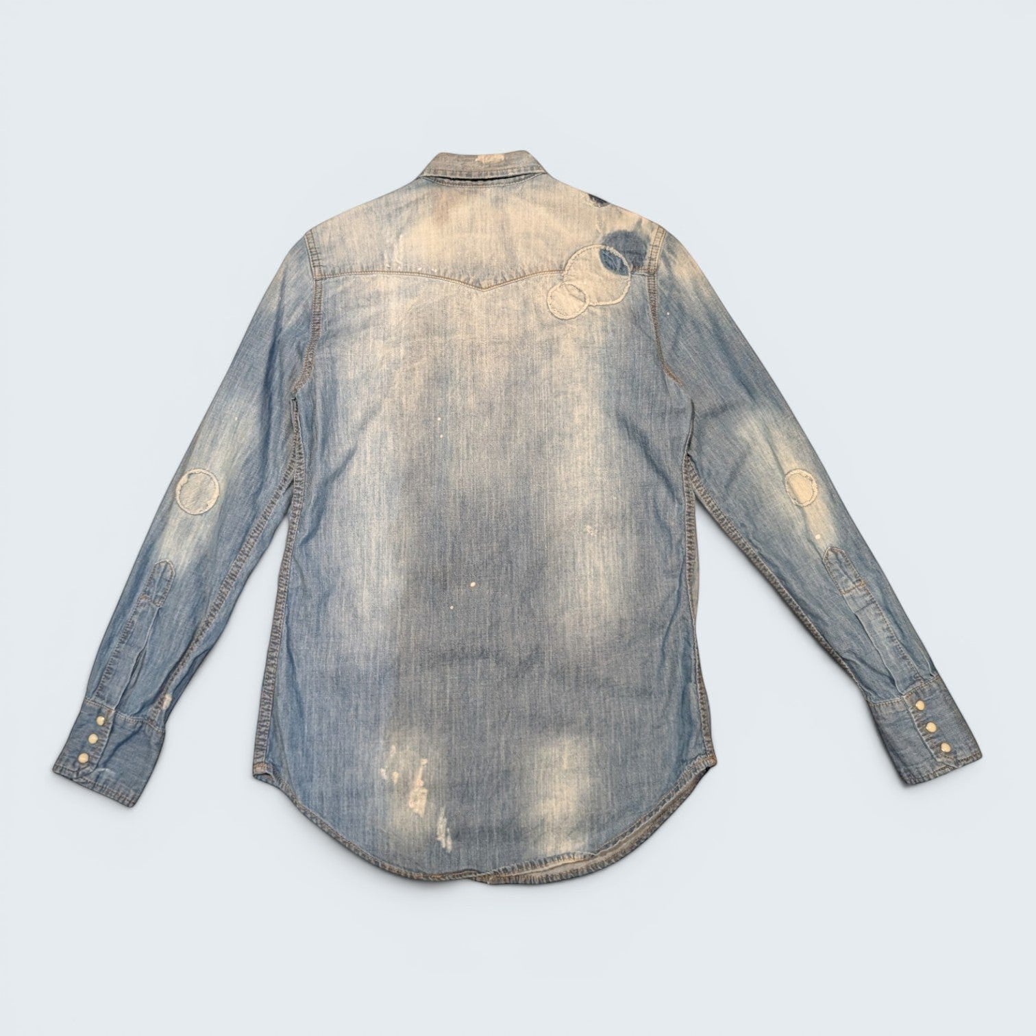 Back view of a light-wash DSQUARED2 denim shirt from STOXX THRIFT & VINTAGE with circular patchwork and distressed details