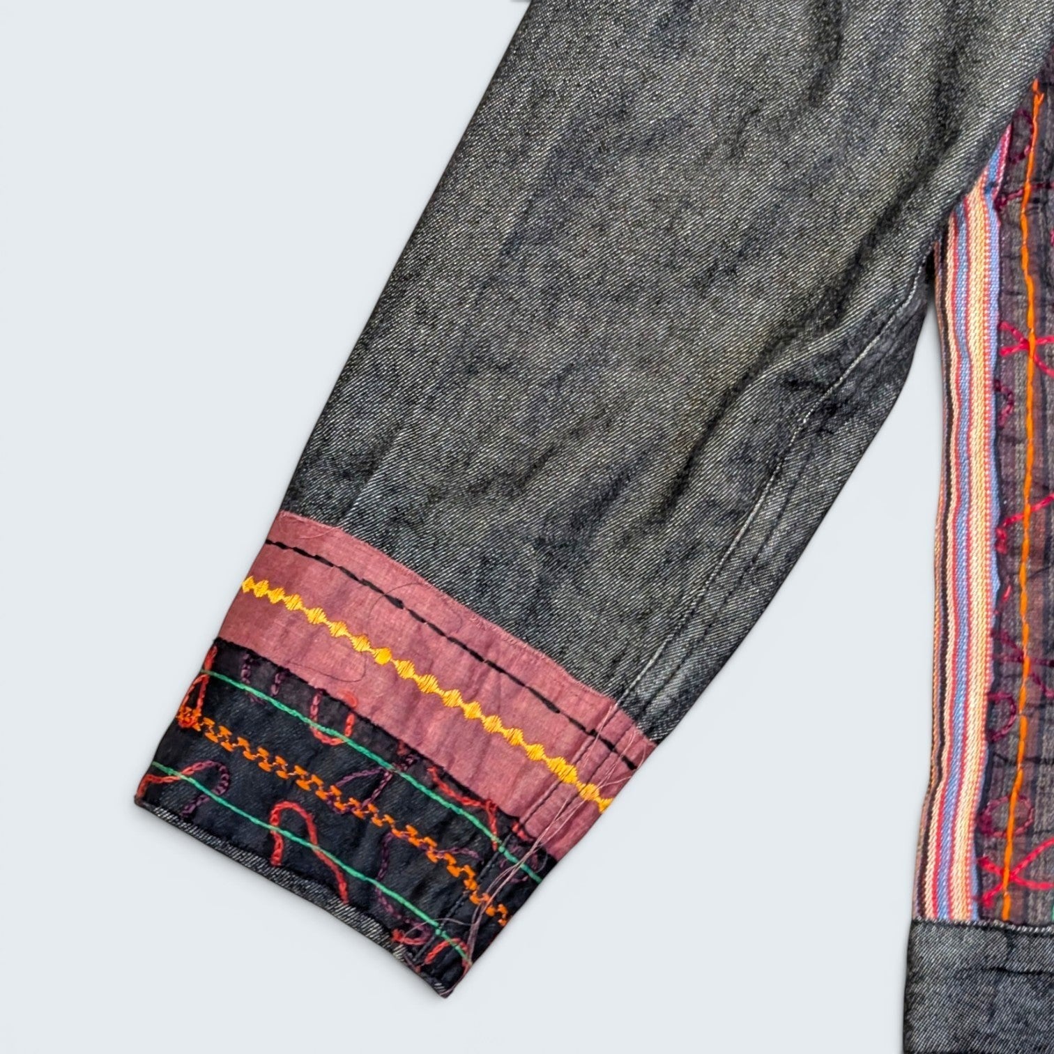 STOXX THRIFT & VINTAGE dark wash denim jacket sleeve with colorful embroidered trim and pink fabric cuff detail.