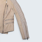 STOXX THRIFT & VINTAGE cream leather biker jacket with quilted sleeves, silver zippers, and asymmetrical closure.